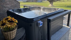 A hot tub with a wooden exterior, a power outlet, and a basket of sunflowers.