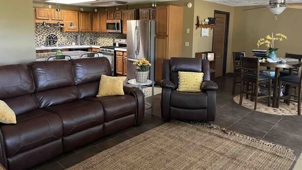 A living room with a brown leather sofa, a dark armchair, and a dining area with wooden chairs and a table.