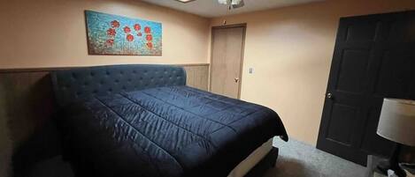 A bedroom with a large bed, a ceiling fan, a door, and a painting on the wall.