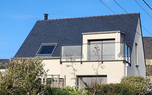 Uma casa moderna com telhado inclinado, varanda com guarda-corpo de vidro e chaminé.