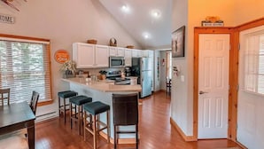 A modern kitchen with white cabinets, a central island with bar stools, and a dining area with a table and chairs. - Your Gateway to Pocono! (Tannersville)