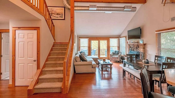 A spacious living area with a wooden staircase, a sofa set, a dining table, and a fireplace. - Your Gateway to Pocono! (Tannersville)