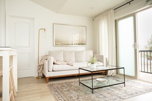 Un salon moderne avec un canapé, une table basse en verre, un lampadaire et une grande fenêtre avec des rideaux.