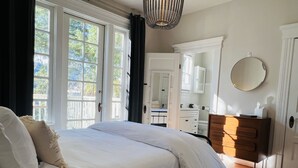 Et soveværelse med en stor seng, et kommode, et spejl og et vindue med gardiner.
