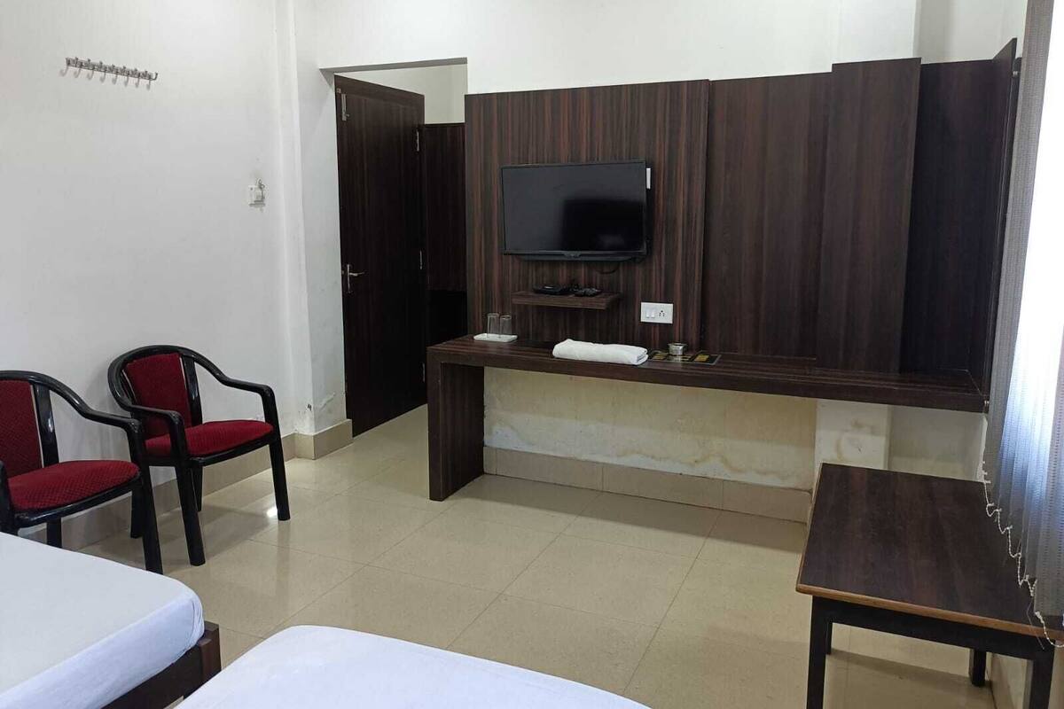 Una habitación de hotel con una cama, un escritorio con televisor, dos sillas rojas y una mesita.