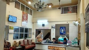 A reception area with a sign indicating check-out time, a chandelier, a television, and a reception desk. - Kusum Hotel And Restaurant (Dibrugarh)