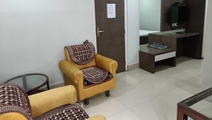 A small, furnished room with a sofa, a desk, and a television. - Kusum Hotel And Restaurant (Dibrugarh)