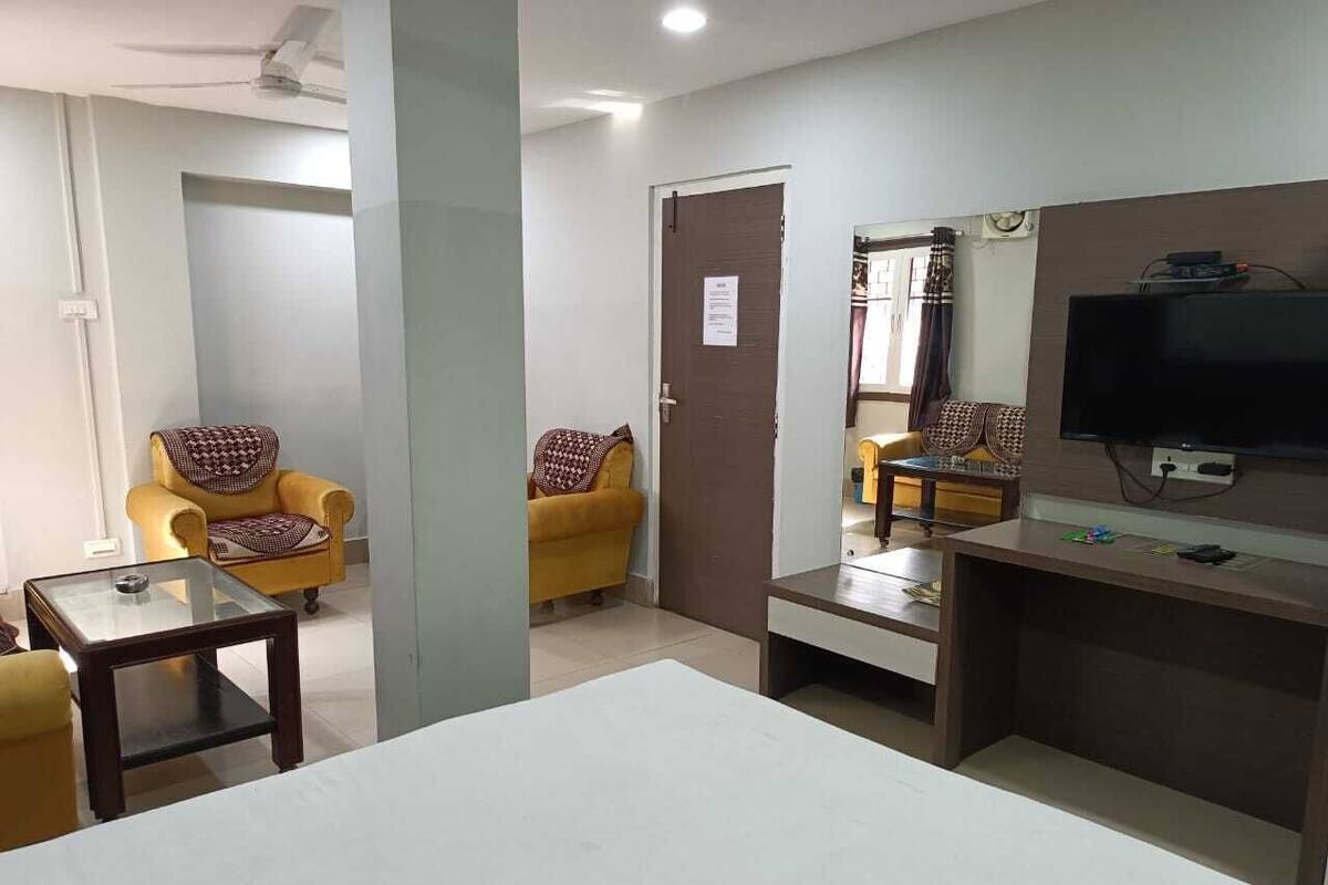 Habitación de hotel con una cama grande, un televisor montado en la pared, una mesita pequeña y dos sillones amarillos.