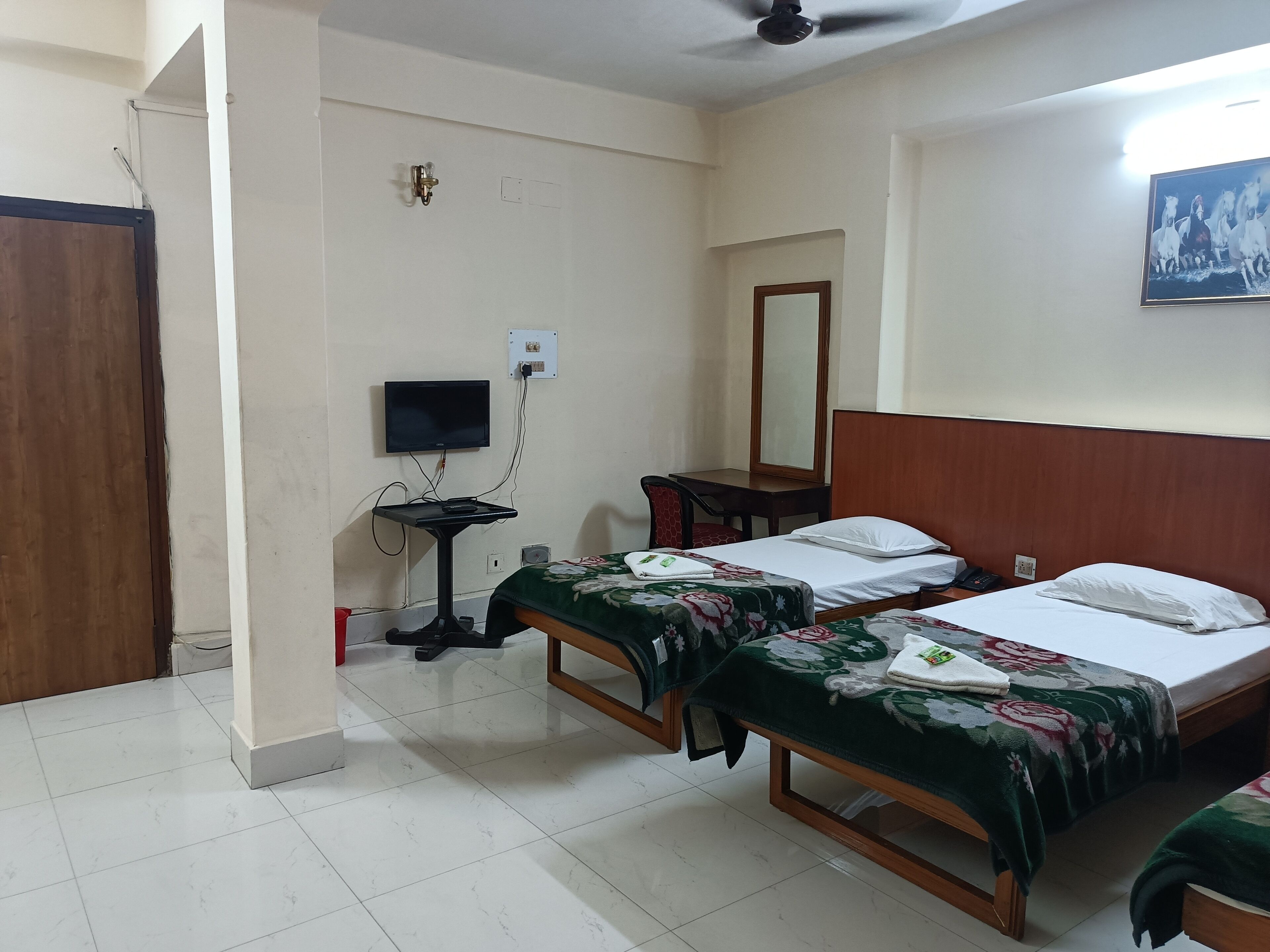A hotel room with two single beds, a desk with a chair, a television, and a mirror on the wall.