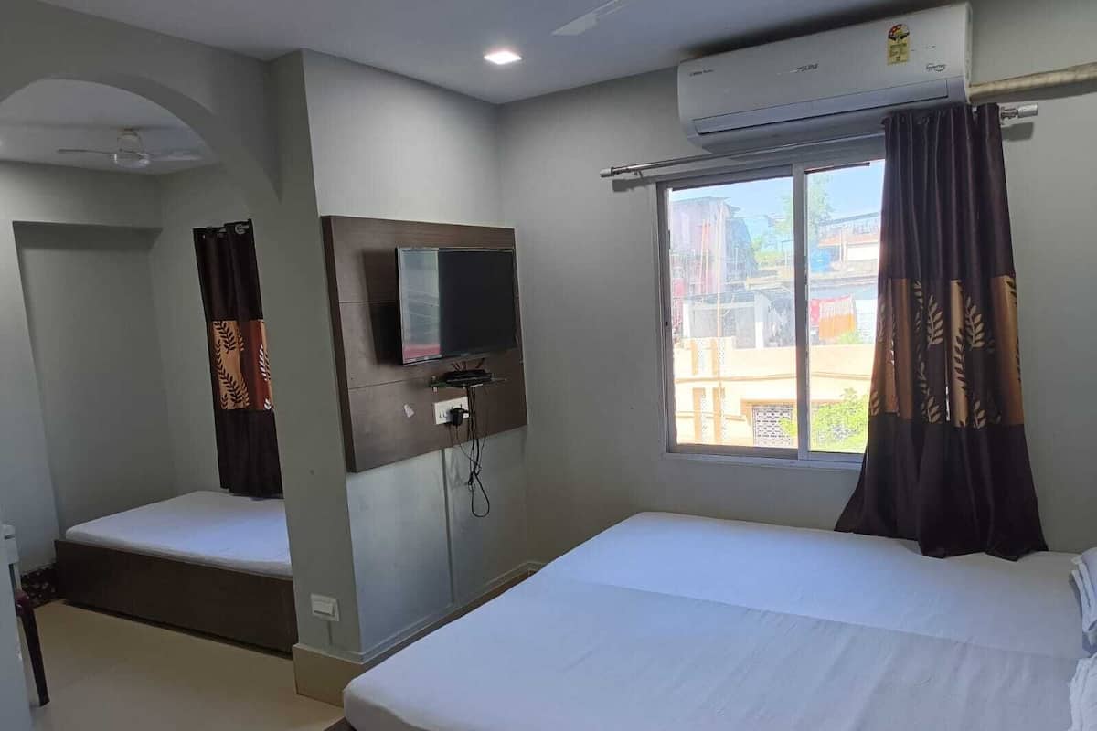 Habitación de hotel con dos camas, un televisor montado en la pared, aire acondicionado y una ventana con cortinas.