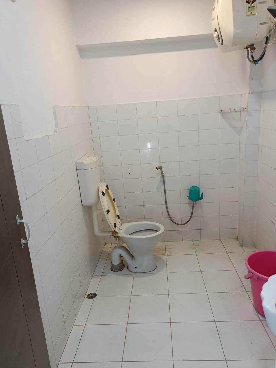 A small, tiled bathroom with a toilet, a shower, and a pink bucket.