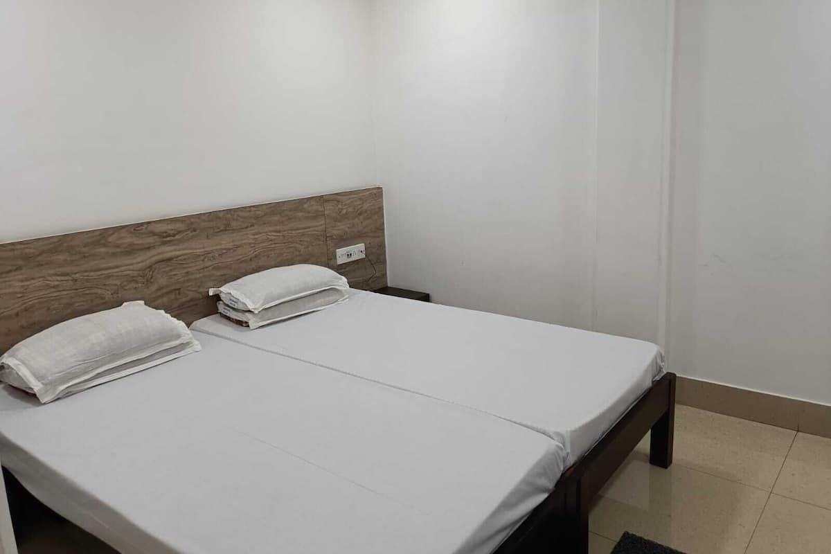 Una cama individual con cabecera de madera en una habitación con paredes blancas y suelo de baldosas.