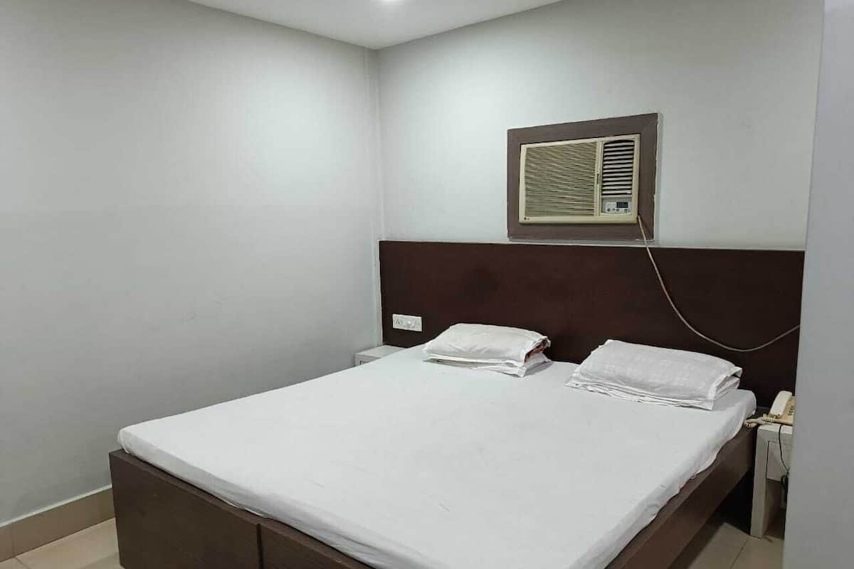 Una cama bien hecha con sábanas blancas, cabecera de madera, aire acondicionado de pared y teléfono en la mesita de noche.
