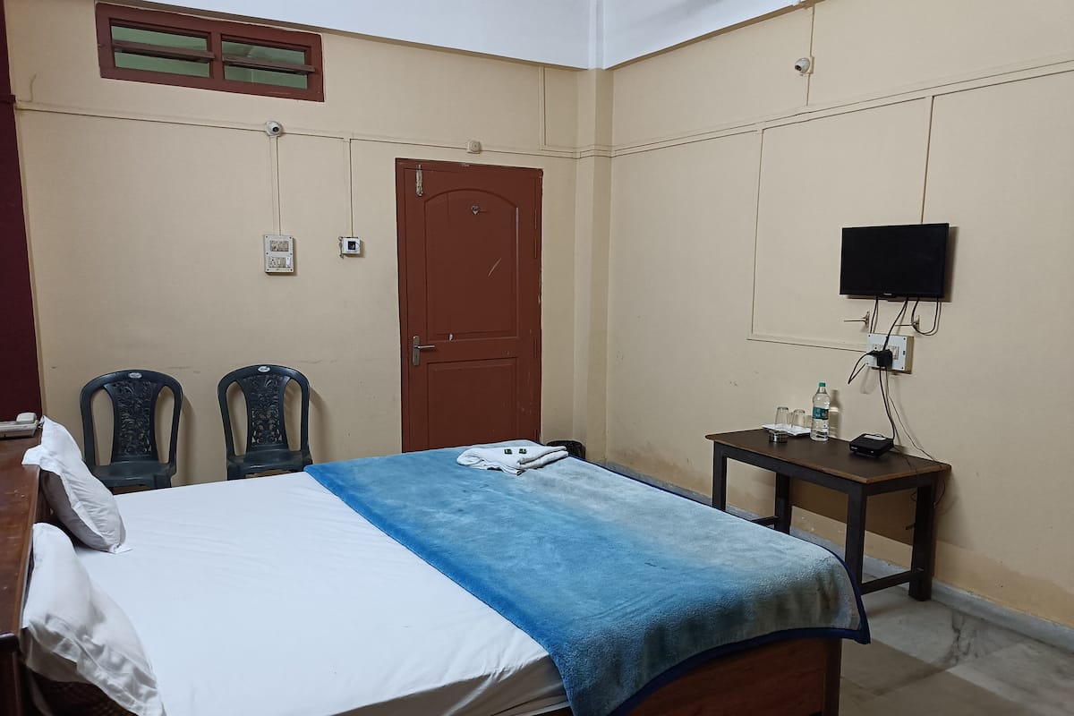Un dormitorio con una cama, dos sillas, una mesa de madera y un televisor, además de una puerta.
