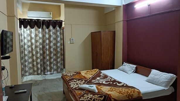 Un dormitorio con cama, un armario de madera, televisor y cortina.