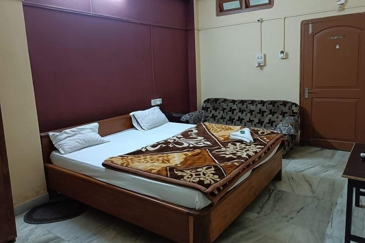 Una cama individual con un edredón estampado, un sofá, una puerta de madera y una mesita.