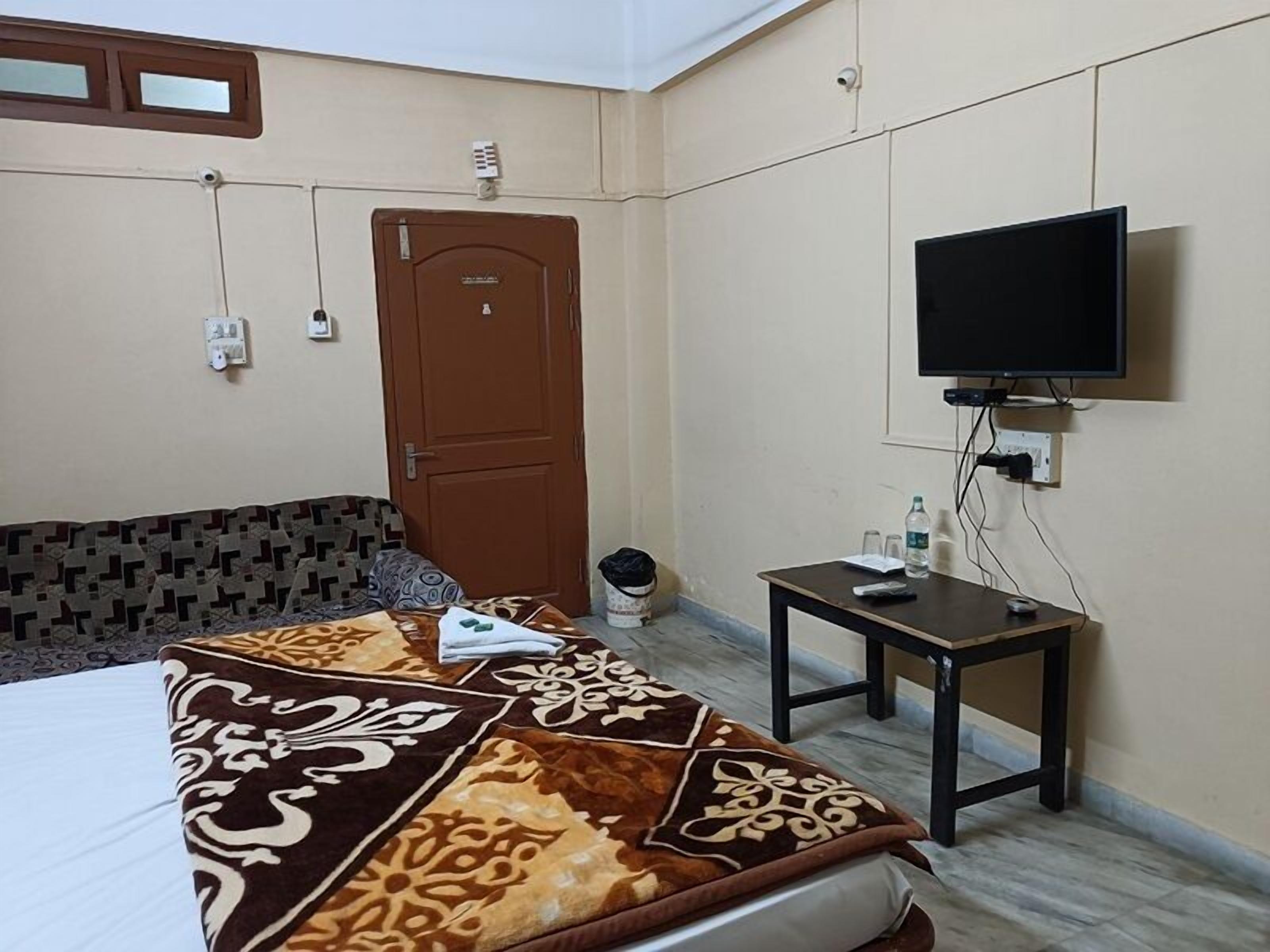 Habitación de hotel con cama, una mesita con televisor, una puerta y una lámpara fijada a la pared.