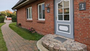 A brick building with a grey door, two windows, and a small garden with flowers. - Haus Friesenglück, Whg. Leuchtturm - Haus Friesenglück (Alkersum)
