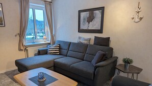 A modern living room with a sectional sofa, a small wooden coffee table, and a side table with a plant. - Haus Friesenglück, Whg. Leuchtturm - Haus Friesenglück (Alkersum)