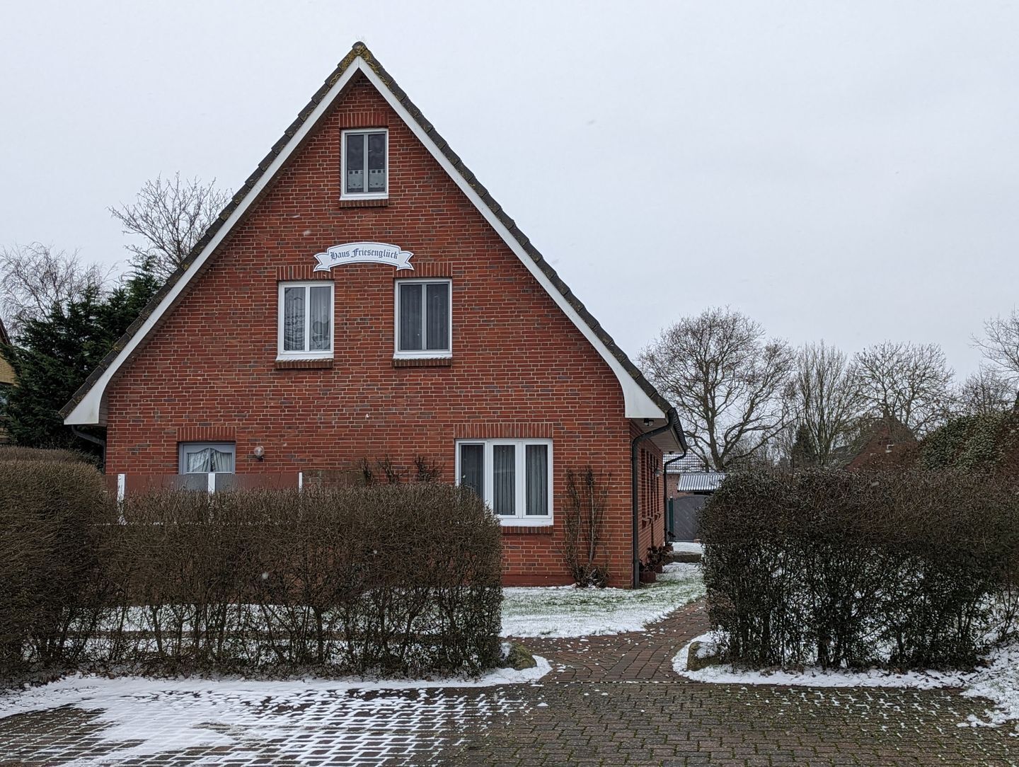 A red brick building with a triangular roof and a sign that reads "Haus Friesengluck".