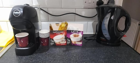 A kitchen counter with a coffee maker, disposable cups, and coffee pods. - Comfy Fenia Stay (London)