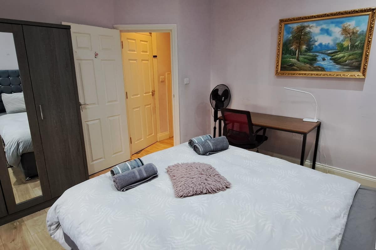 Une chambre à coucher comprenant un lit, un bureau, une chaise, une armoire, un miroir, un tableau et une lampe de sol.