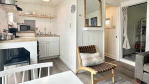 A modern kitchen with white cabinetry, a microwave, and a sink. There is a wooden bench with a cushion in the living area.