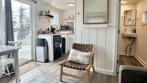 A compact kitchen with a microwave, toaster, and dishwasher, a wooden chair with a cushion, and a dining area with a table and chairs.