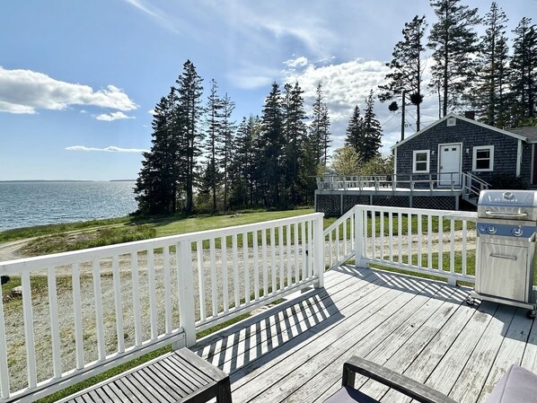 A wooden deck with a white railing, a grill, and a small cabin-like structure.