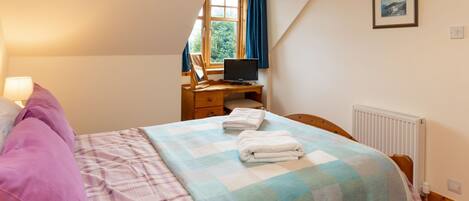 Ein Schlafzimmer mit Bett, Schreibtisch mit Computer, Fenster mit Vorhängen und Heizkörper.