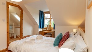 A bedroom with a large bed, a desk, a mirror, and a window with curtains. - Osprey House by Interhome (Nethy Bridge)
