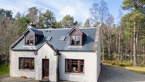 A two-story house with a stone facade, a gravel driveway, and a forested backdrop. - Osprey House by Interhome (Nethy Bridge)