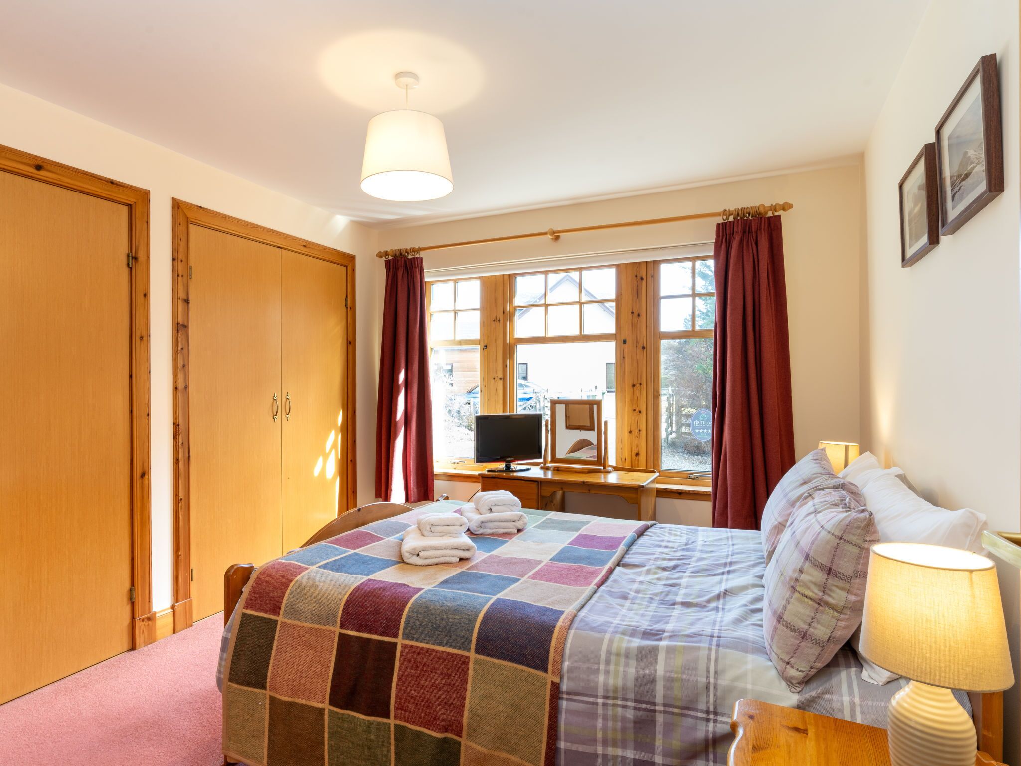 A bedroom with a bed, a desk with a computer, a window with curtains, and a wardrobe.