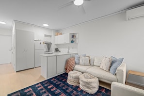 Un espace de vie compact comprenant un coin cuisine, un canapé avec des coussins et un tapis à motifs.