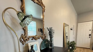 Une pièce avec un meuble en bois foncé, un miroir à cadre doré, une lampe verte et une petite plante en pot.