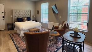 Une chambre à coucher avec un lit, une chaise, une petite table et un téléviseur fixé au mur.