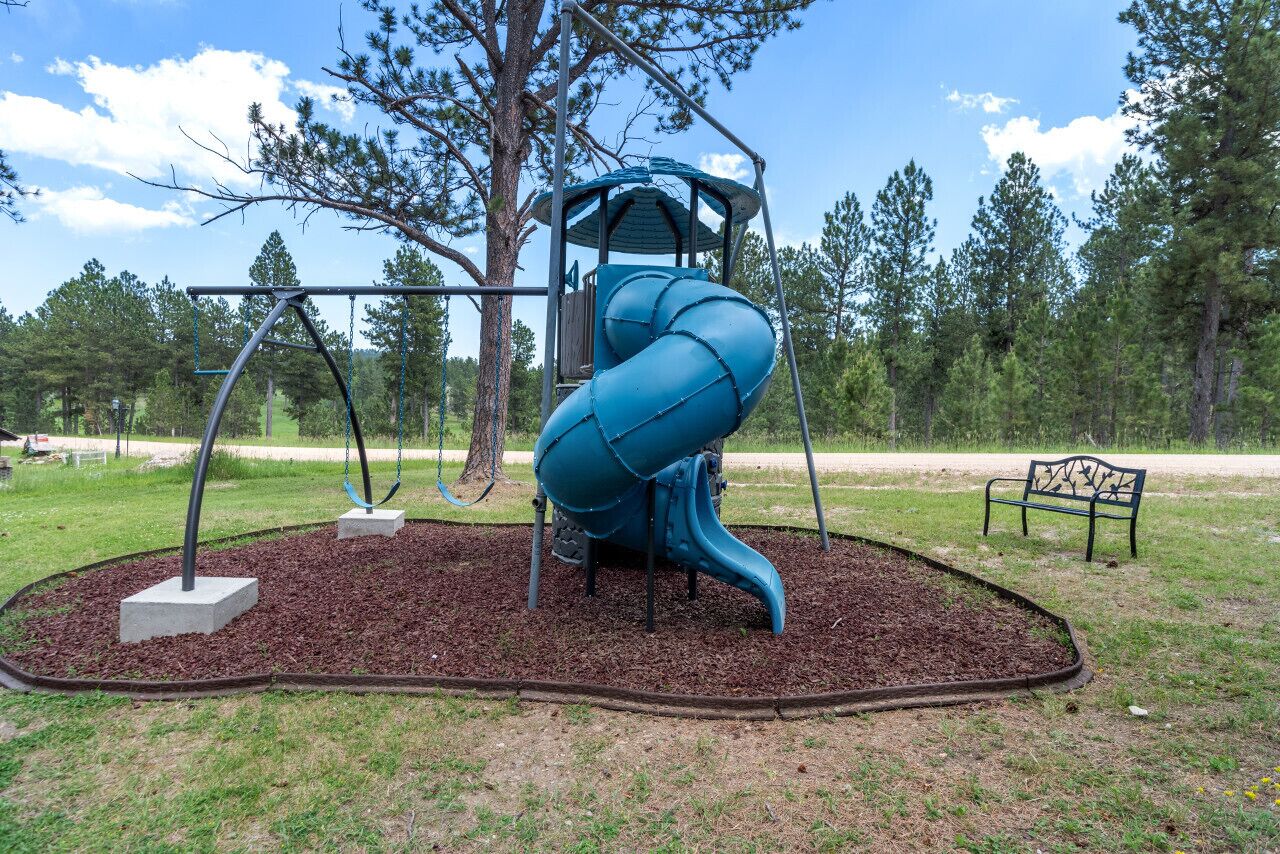 A playground with a blue spiral slide, swings, and a bench.