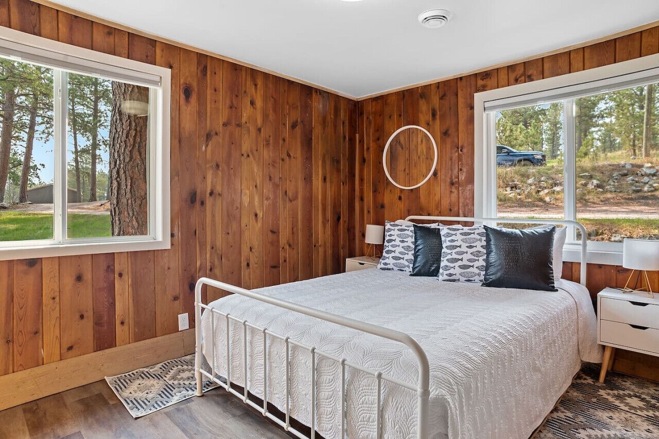 A bedroom with a large bed, wooden walls, and a view of the outdoors.