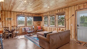 A wooden cabin interior with a sofa, chairs, a table, and a TV.