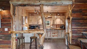 A rustic kitchen with wooden walls and a central island with stools.