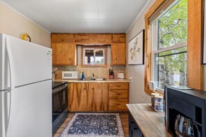 A compact kitchen with wooden cabinets, a microwave, a sink, and a window with a view of trees.