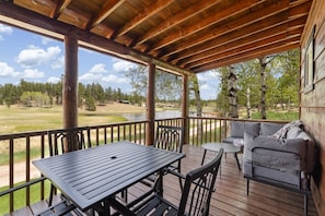 Uma área externa coberta com mesa, cadeiras, sofá e vista para um lago e árvores.