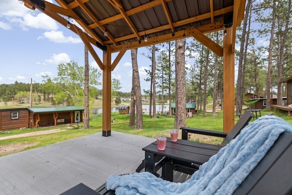 A covered outdoor seating area with a view of a lake and cabins.