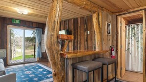A rustic interior with a wooden wall, a bench, an exit sign, and a view through a glass door. - Little Joy: Needle Spire Views + Sauna + Wildlife (Custer)
