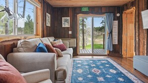 A cozy cabin interior with a sofa, a patterned rug, and a view of the outdoors through a glass door. - Little Joy: Needle Spire Views + Sauna + Wildlife (Custer)