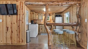 Eine rustikale Küche mit Holzwänden, einem zentralen Holzbalken und Barhocker.