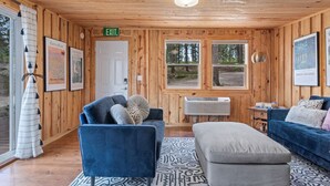 Ein Interieur einer Holzhütte mit einem blauen Sofa, einem grauen Hocker und einer weißen Tür mit der Aufschrift 'EXIT'.