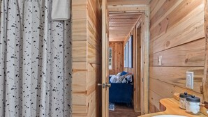 Ein Holzhütten-Innenraum mit Bad, einem Bett mit blauer Bettwäsche und einer Holzauslage mit Gläsern.