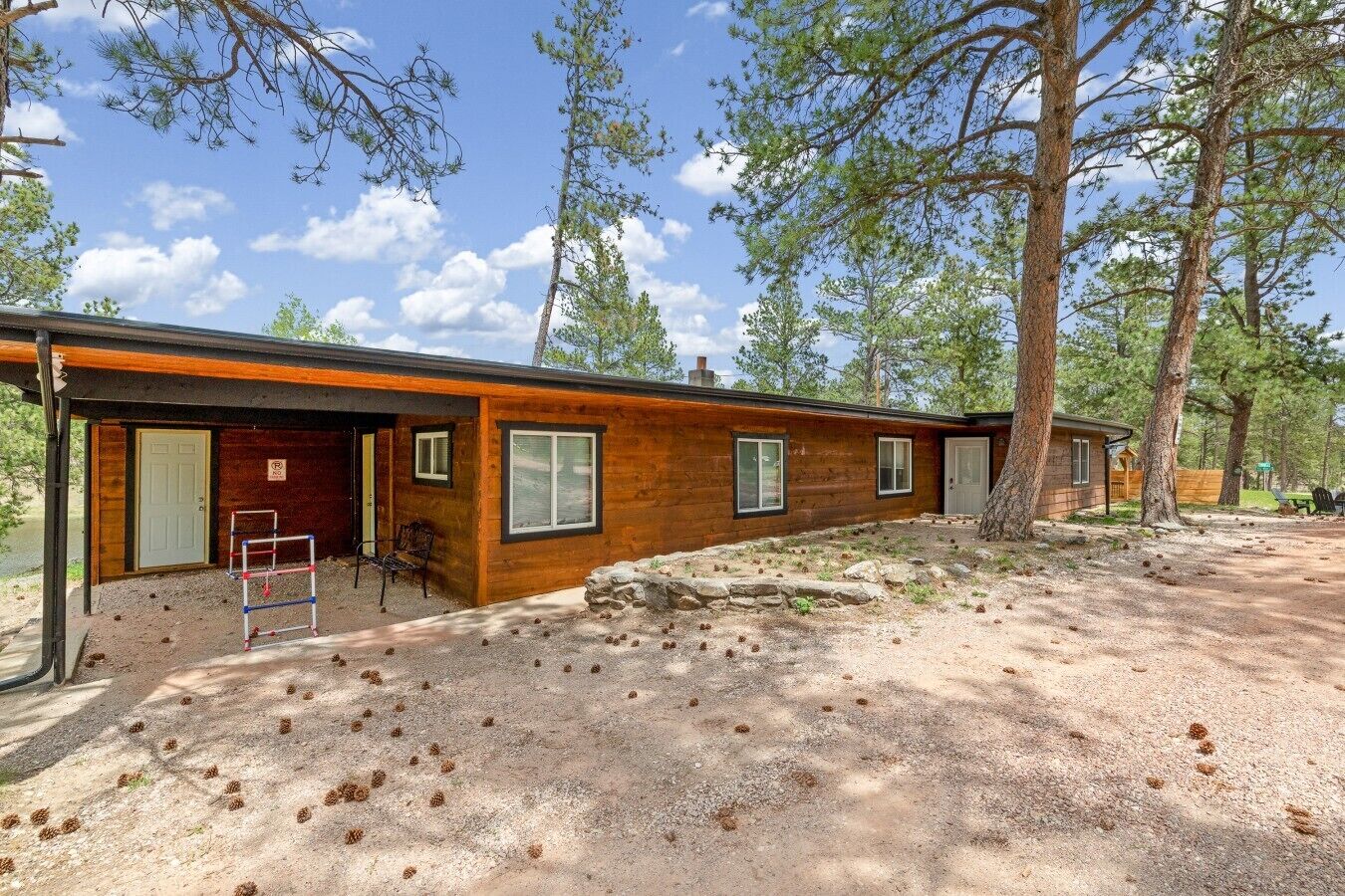 A cabin with a covered porch, a small outdoor seating area, and a gravel driveway.