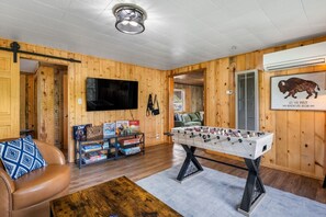 A cozy room with wooden walls, a foosball table, a TV, and a sofa.